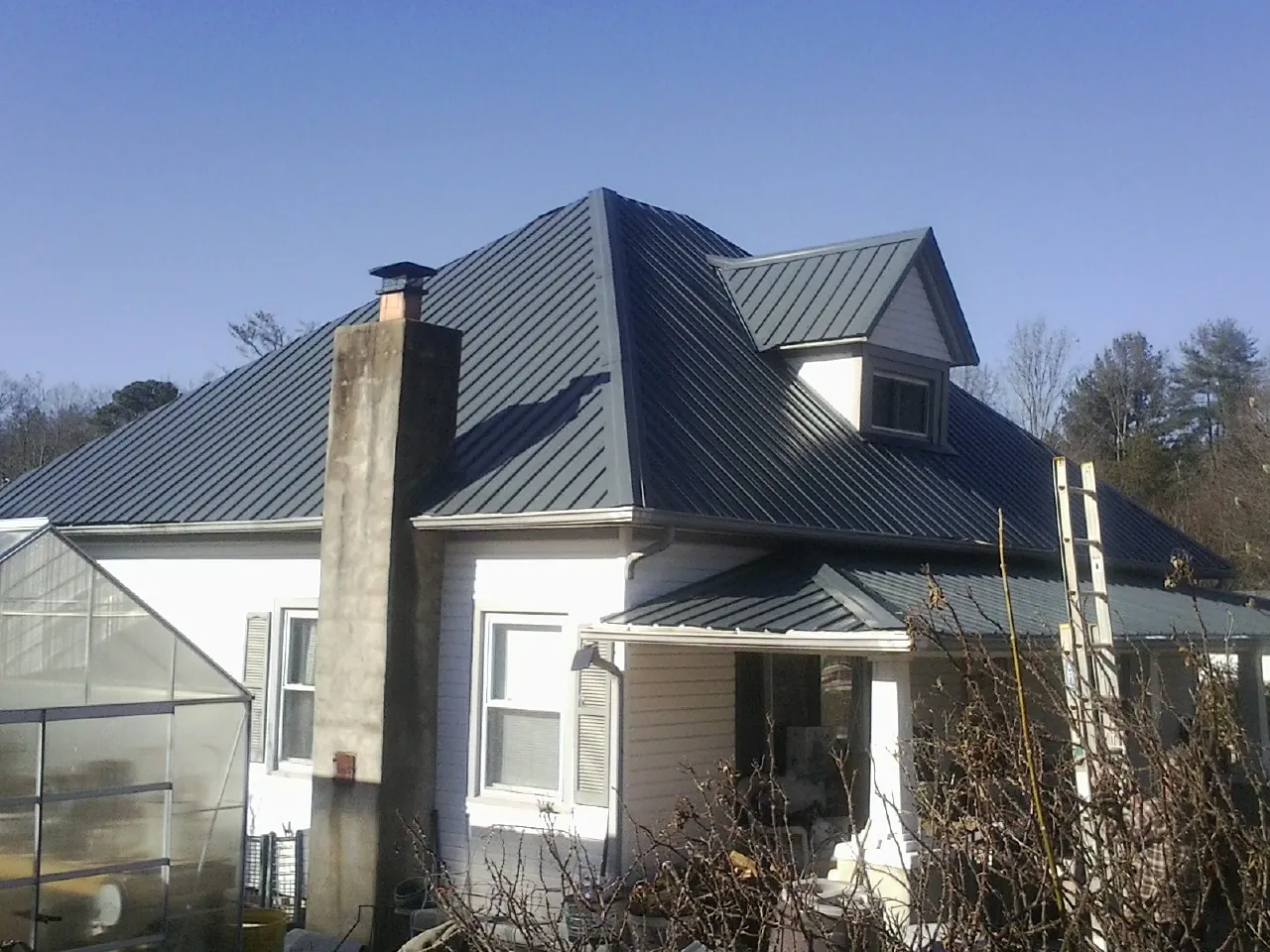 Dark blue standing seam metal roof on a white farmhouse with dormer — Slate & Tile Roof Repair by Roofing Brothers in Two Rivers