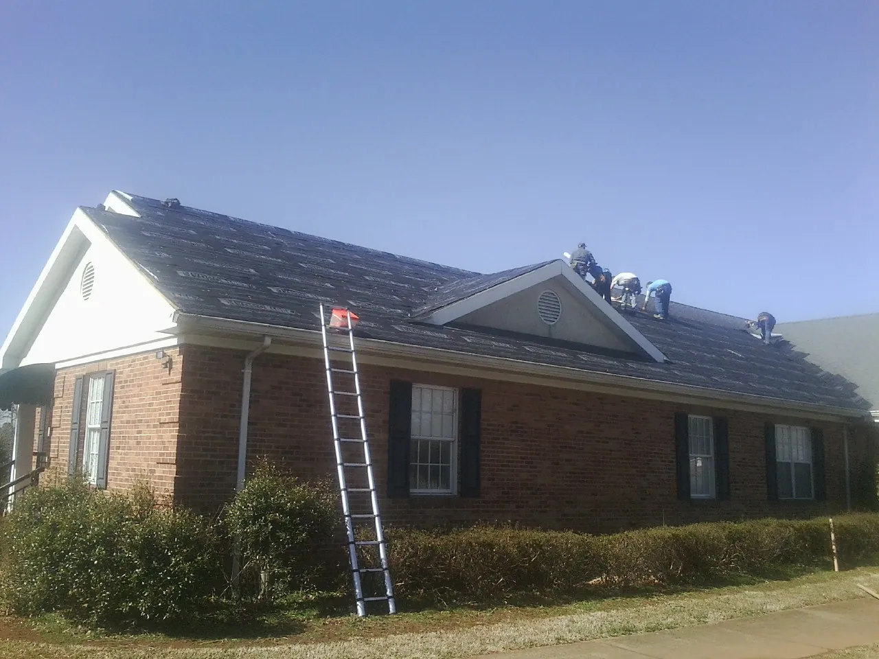 Crew tearing shingles off a brick ranch roof with a ladder set — Emergency Roof Repair work by our crew in Two Rivers