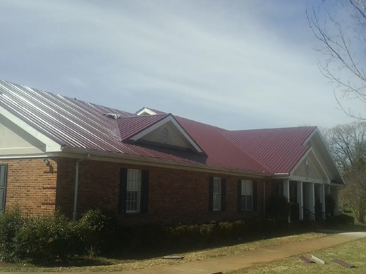 Red metal roof with gabled entries on a long brick building, from a Hail Damage Roof Repair job in Two Rivers