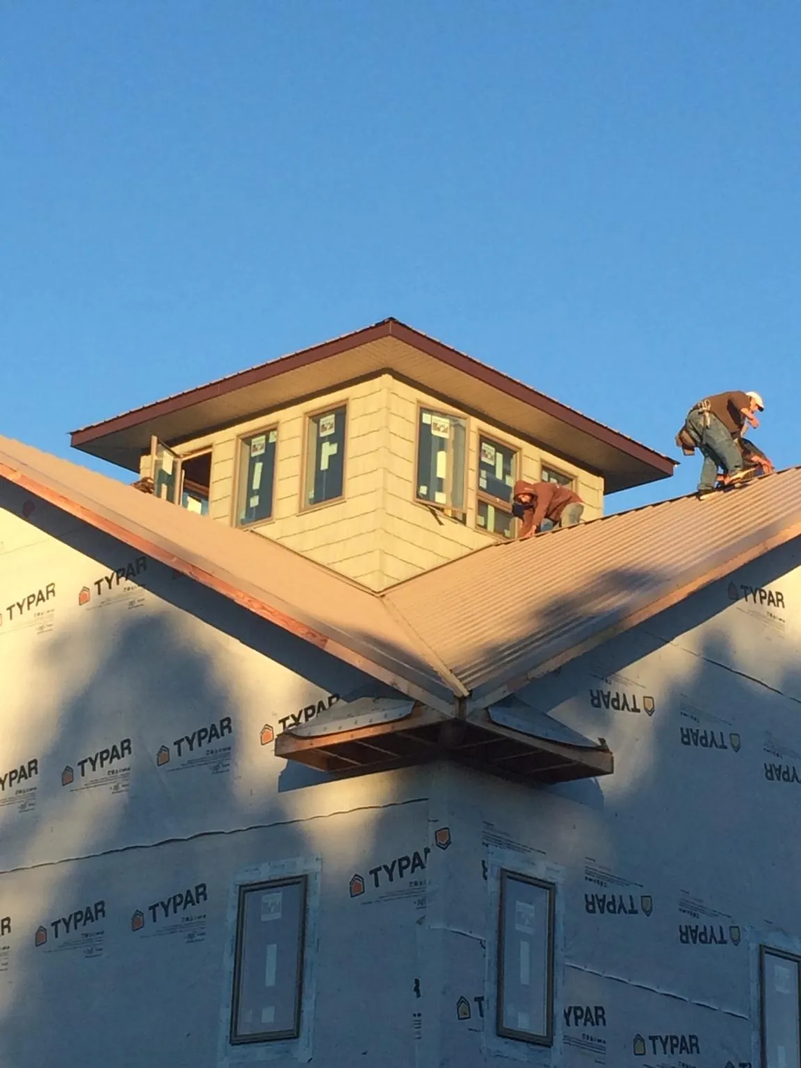 Roofers working around a rooftop cupola on a new metal roof at sunset — Roof Waterproofing in Two Rivers by Roofing Brothers